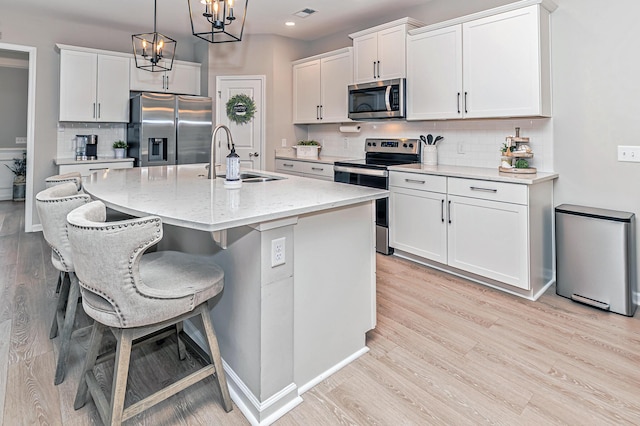 kitchen with light wood-type flooring, a sink, white cabinetry, stainless steel appliances, and an inviting chandelier