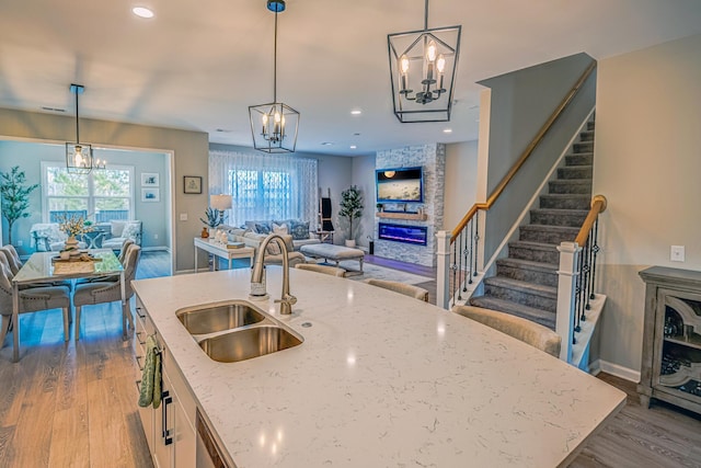 kitchen featuring a sink, open floor plan, a fireplace, a notable chandelier, and a kitchen island with sink