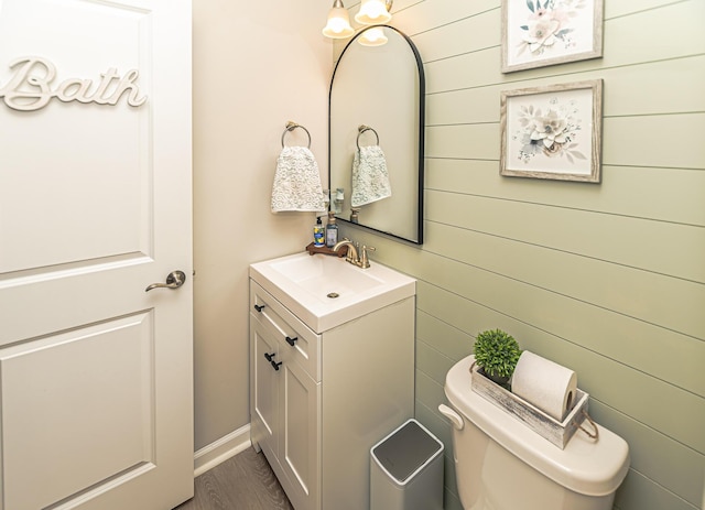 half bath with wooden walls, toilet, vanity, and wood finished floors