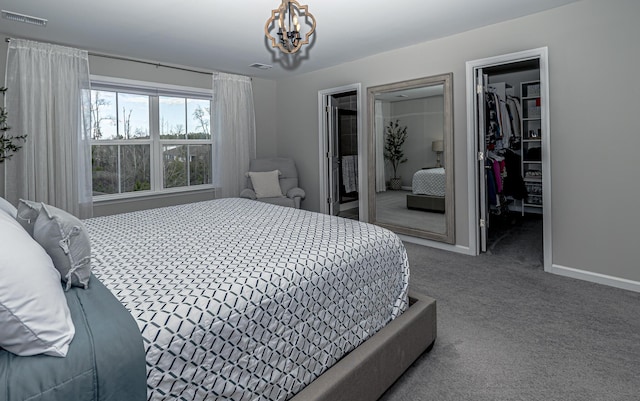 carpeted bedroom featuring a walk in closet, baseboards, visible vents, and a chandelier