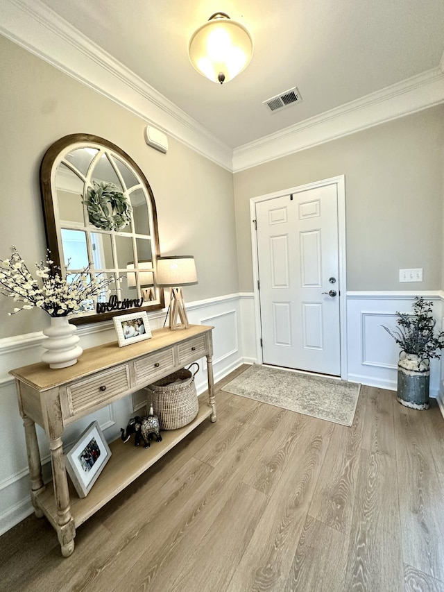 entrance foyer with visible vents, a wainscoted wall, wood finished floors, and crown molding