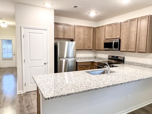 kitchen with light stone counters, kitchen peninsula, hardwood / wood-style floors, appliances with stainless steel finishes, and sink