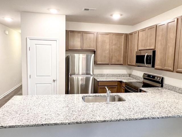 kitchen with stainless steel appliances, sink, light stone counters, and kitchen peninsula