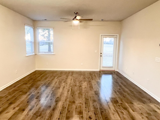 empty room featuring ceiling fan, a wealth of natural light, and dark wood-type flooring