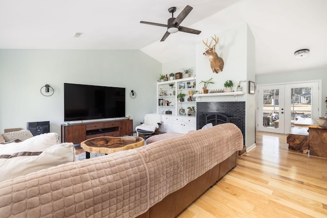 living room featuring french doors, vaulted ceiling, light hardwood / wood-style flooring, ceiling fan, and a fireplace