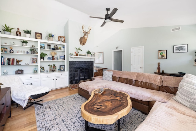 living room featuring lofted ceiling, a fireplace, ceiling fan, and light wood-type flooring