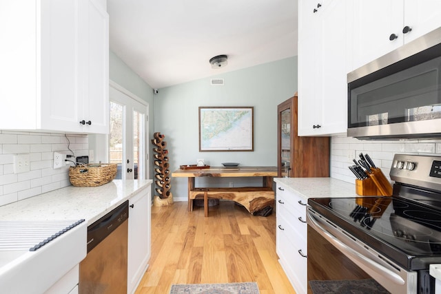 kitchen featuring lofted ceiling, appliances with stainless steel finishes, light stone counters, light hardwood / wood-style floors, and white cabinets