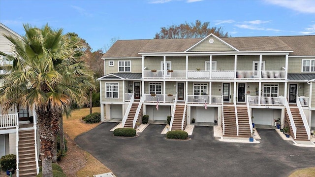 view of front of home featuring driveway, an attached garage, a standing seam roof, covered porch, and stairs