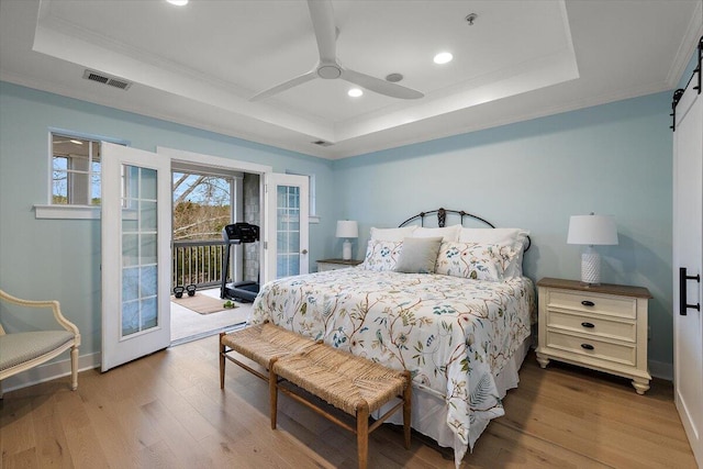 bedroom with a barn door, visible vents, wood finished floors, access to exterior, and a tray ceiling