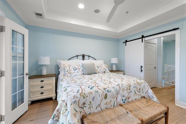 bedroom with a barn door, wood finished floors, visible vents, ornamental molding, and a tray ceiling