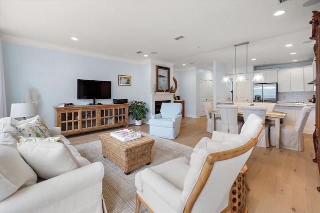 living area featuring light wood-style flooring, a fireplace, visible vents, and crown molding