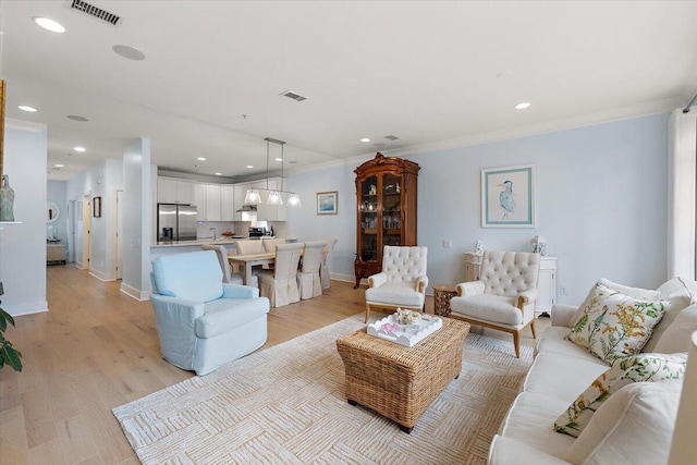 living room featuring light wood finished floors, visible vents, and crown molding