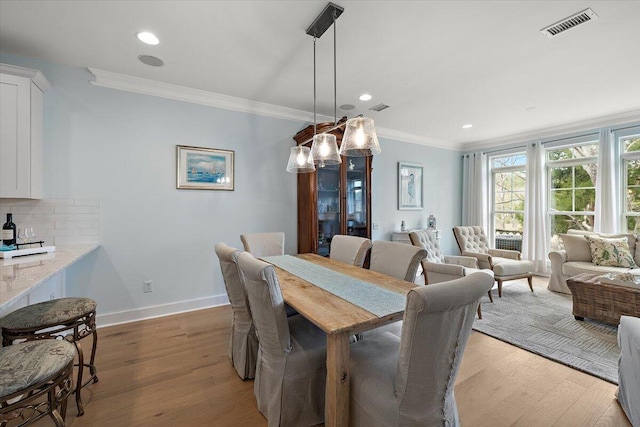 dining room featuring baseboards, light wood-type flooring, visible vents, and crown molding