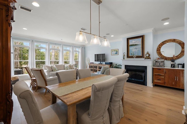 dining area with light wood-type flooring, a fireplace, visible vents, and crown molding