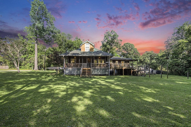 back of property at dusk featuring stairs, a lawn, and a deck