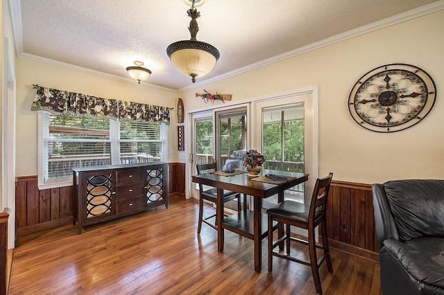 dining area featuring a textured ceiling, wood finished floors, ornamental molding, and wainscoting