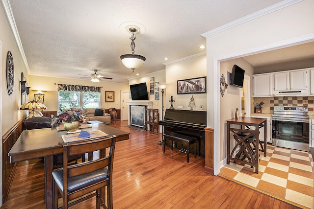 dining room with light wood-style flooring, crown molding, a ceiling fan, a fireplace, and a textured ceiling