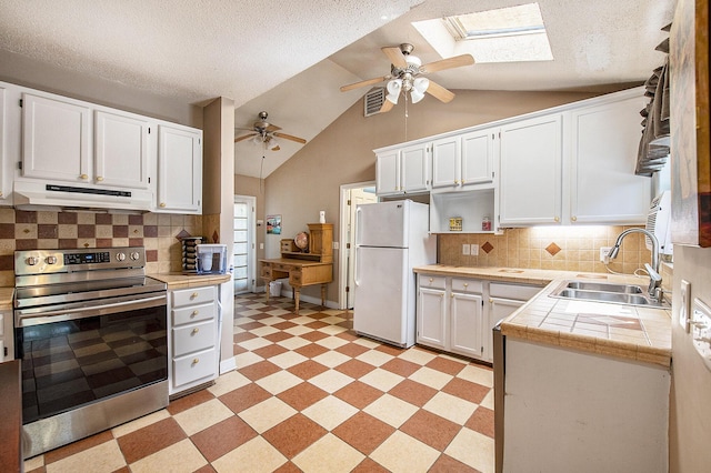 kitchen with under cabinet range hood, stainless steel electric stove, freestanding refrigerator, a sink, and light floors