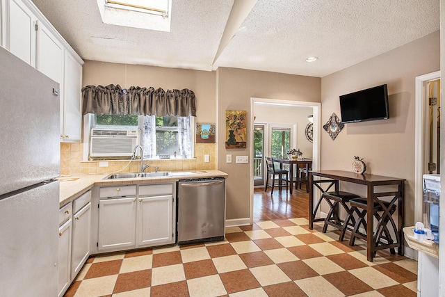 kitchen featuring freestanding refrigerator, stainless steel dishwasher, a sink, light countertops, and white cabinetry