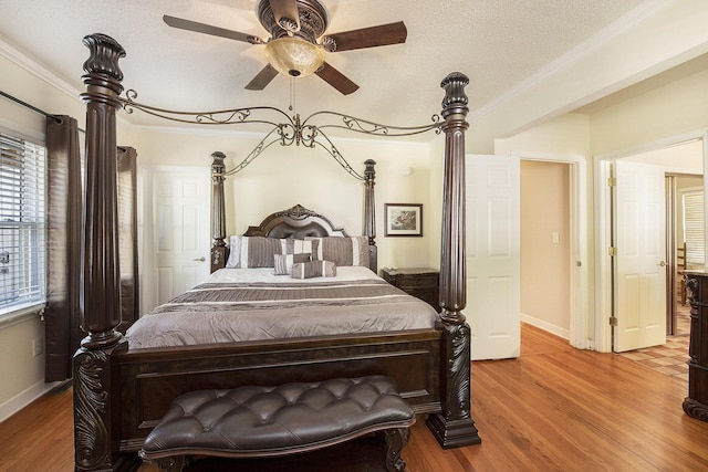 bedroom with wood finished floors, ornamental molding, baseboards, a textured ceiling, and a ceiling fan