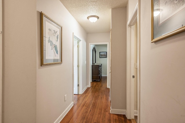 hall with wood finished floors, a textured ceiling, and baseboards