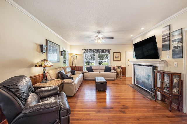living room featuring wood finished floors, crown molding, a ceiling fan, a fireplace with flush hearth, and a textured ceiling