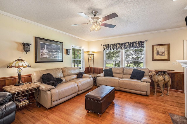 living area with a textured ceiling, a wainscoted wall, wood finished floors, crown molding, and ceiling fan
