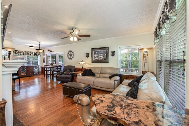 living room featuring a textured ceiling, a ceiling fan, wood finished floors, crown molding, and a fireplace