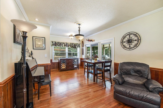 living area with a wainscoted wall, wood walls, light wood-type flooring, a textured ceiling, and ornamental molding