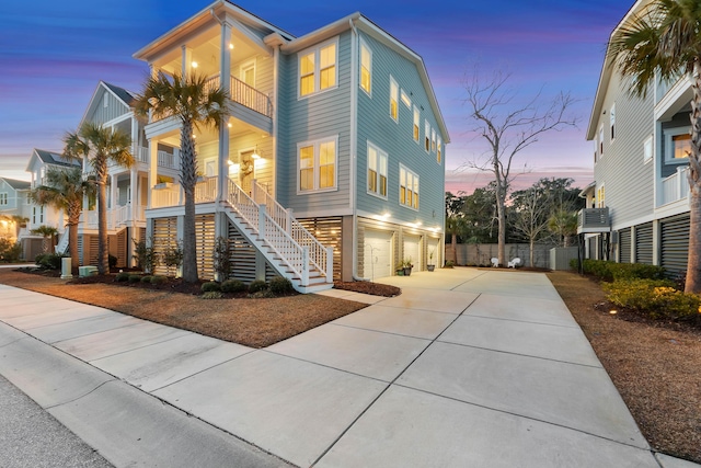 coastal home with a porch, driveway, a balcony, an attached garage, and stairs