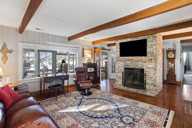 living area featuring visible vents, beamed ceiling, wood-type flooring, a decorative wall, and a brick fireplace