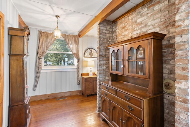 interior space featuring crown molding, wood finished floors, brick wall, baseboards, and visible vents