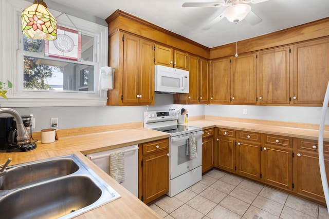 kitchen featuring brown cabinets, light countertops, light tile patterned floors, a sink, and white appliances