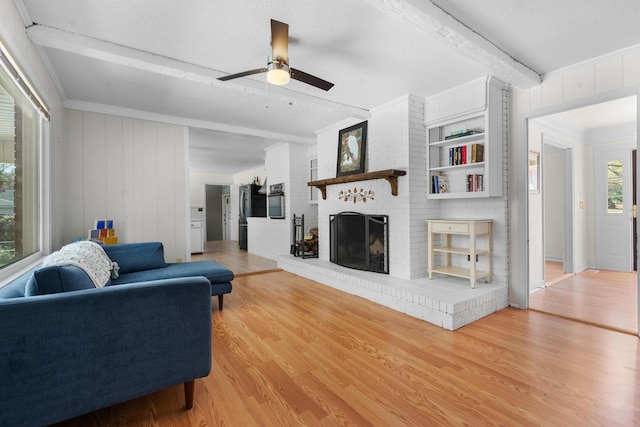 living room featuring ceiling fan, beam ceiling, a fireplace, ornamental molding, and wood-type flooring