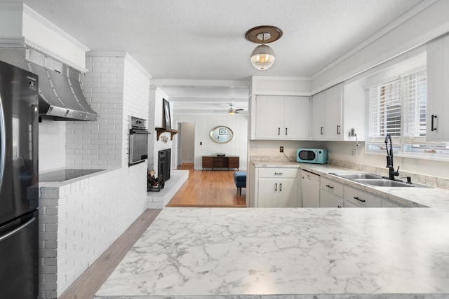 kitchen featuring sink, black appliances, a brick fireplace, hanging light fixtures, and white cabinets