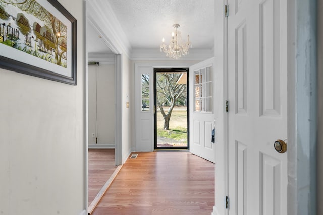 entrance foyer featuring an inviting chandelier, ornamental molding, a textured ceiling, and hardwood / wood-style flooring