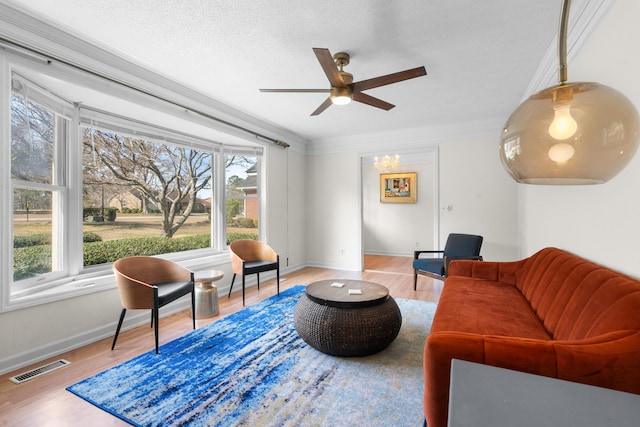 living room featuring crown molding, ceiling fan, light hardwood / wood-style flooring, and a textured ceiling