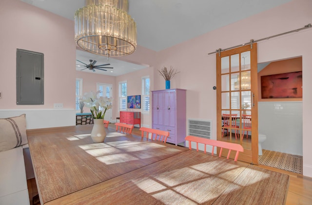 dining space with hardwood / wood-style floors, electric panel, a barn door, and ceiling fan with notable chandelier