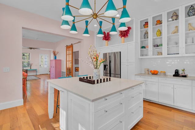 kitchen with white cabinets, decorative light fixtures, light wood-type flooring, stainless steel refrigerator with ice dispenser, and a center island