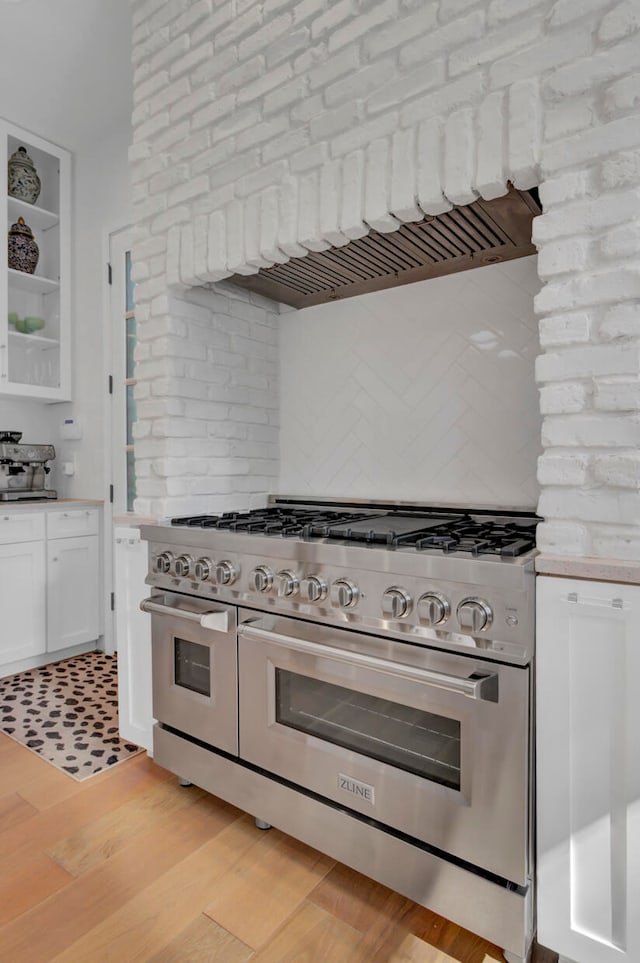 kitchen featuring custom exhaust hood, white cabinetry, light wood-type flooring, double oven range, and brick wall