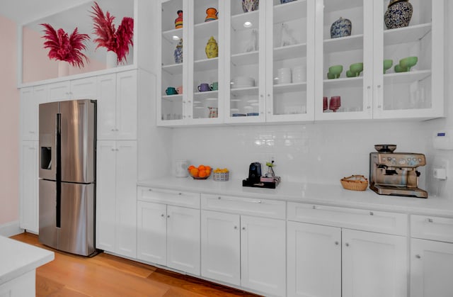 kitchen featuring light hardwood / wood-style floors, stainless steel fridge, white cabinets, and backsplash