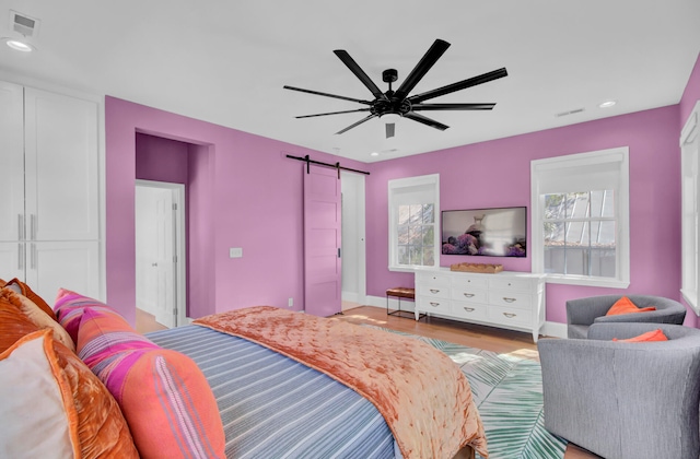 bedroom with light hardwood / wood-style floors, multiple windows, a barn door, and ceiling fan