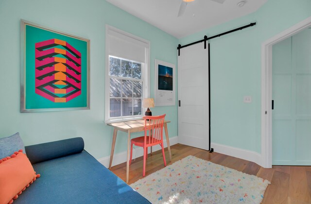 home office with a barn door, light wood-type flooring, and ceiling fan