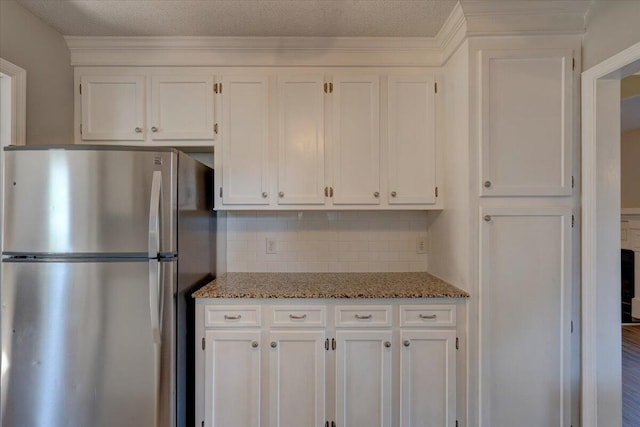 kitchen featuring backsplash, stainless steel refrigerator, stone countertops, and white cabinetry