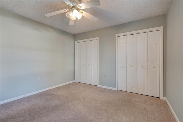 unfurnished bedroom featuring ceiling fan, two closets, a textured ceiling, and light carpet