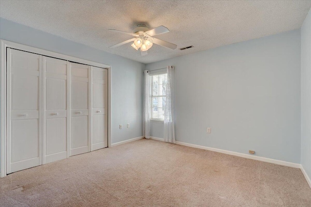 unfurnished bedroom with ceiling fan, a textured ceiling, a closet, and light carpet