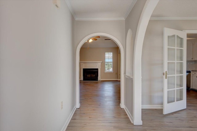 hallway with light wood-type flooring, french doors, ornamental molding, and a textured ceiling