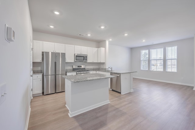 kitchen featuring light stone counters, white cabinetry, a center island, kitchen peninsula, and stainless steel appliances