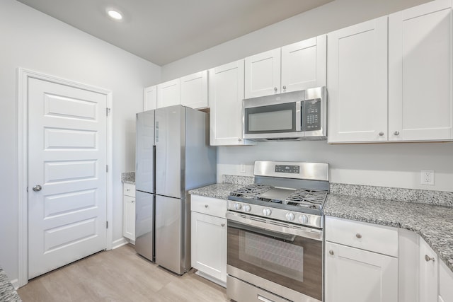 kitchen with stainless steel appliances, white cabinetry, and light stone countertops