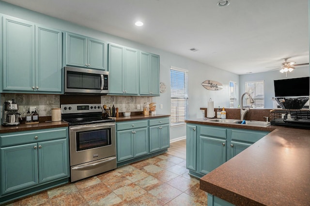 kitchen with dark countertops, appliances with stainless steel finishes, backsplash, a sink, and green cabinetry